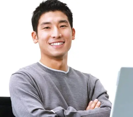 Asian person smiling with arms folded in front of partially visible laptop screen